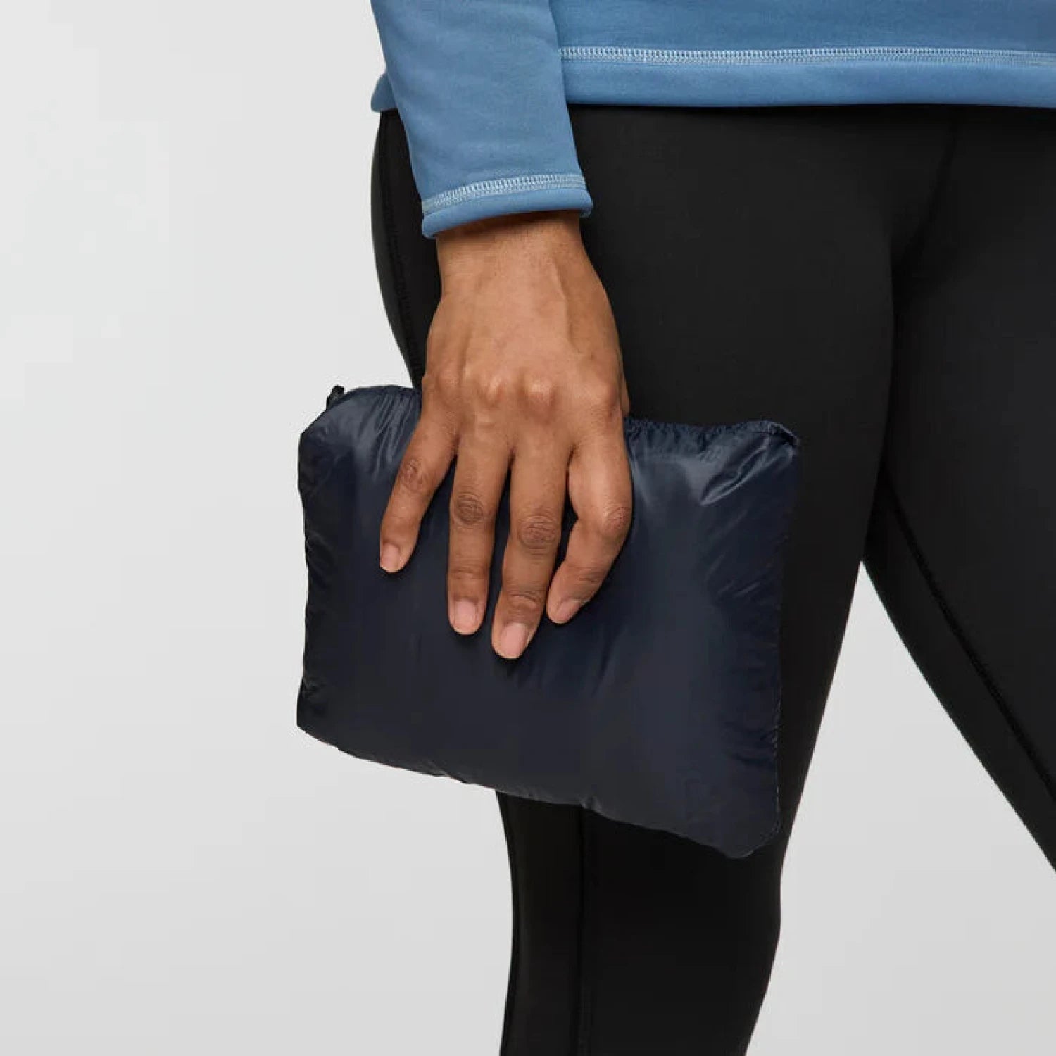 Person holding a black folded jacket against a light gray background