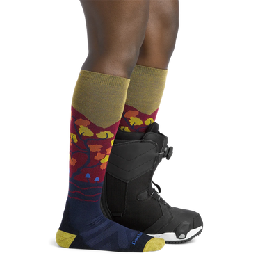 Darn Tough Womens's Enchanted Over-the-Calf Midweight Ski & Snowboard Sock shown in the Autumn design. Shown on model.