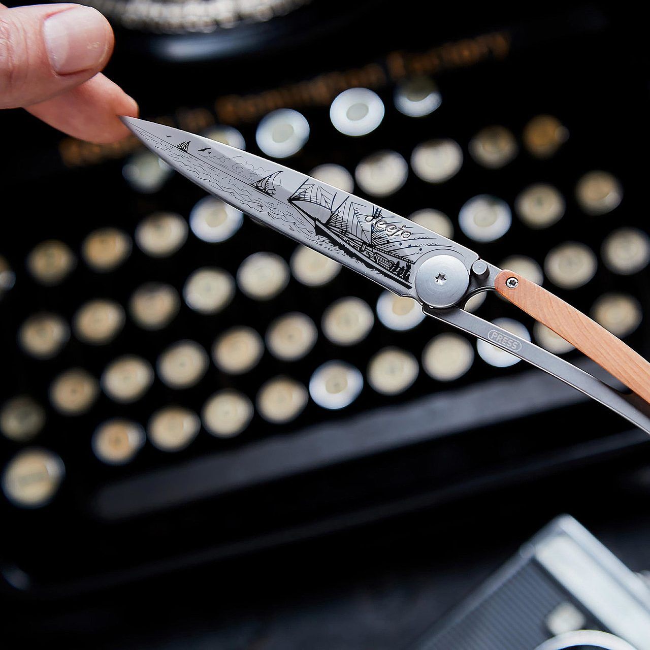 deejo 37g olive wood sailing knife held in front of typewriter 