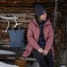 fjallraven womens kiruna padded parka jacket in port color front view worn by model sitting on a wooden bench near snow