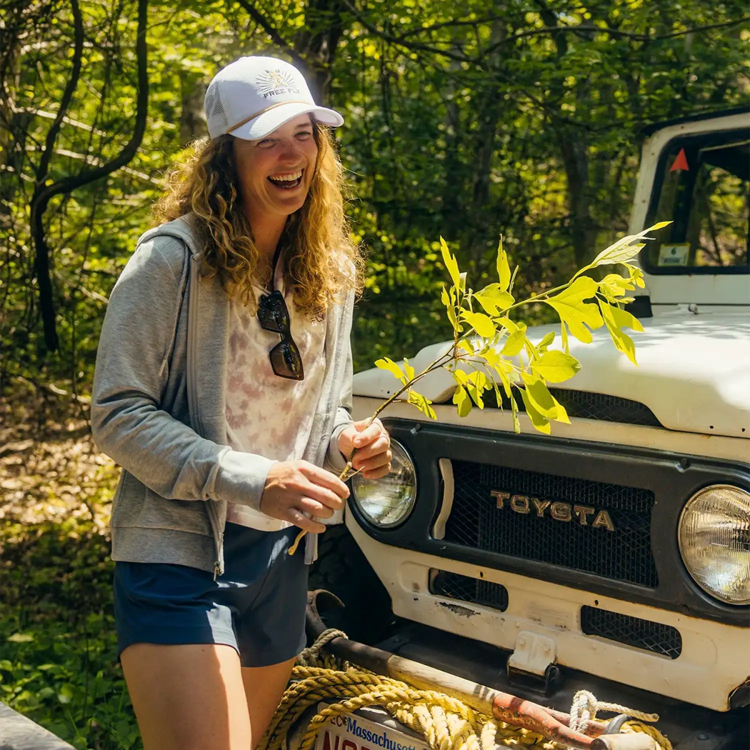 free fly womens bamboo lightweight fleece zip hoodie in light heather grey model next to car in forest 