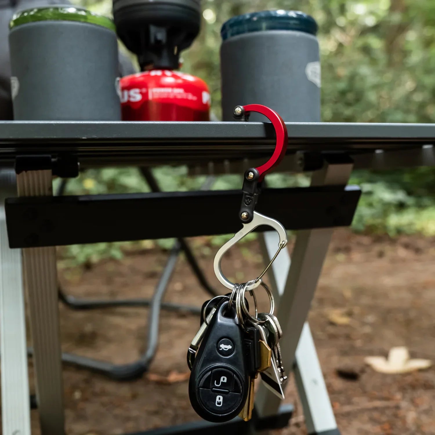 small gear clip with keys and car fob attached, hanging off edge of camping table 