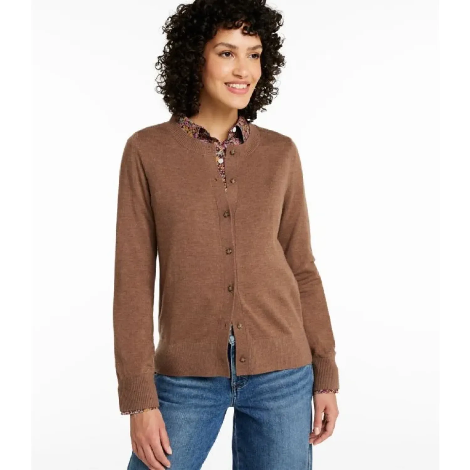 Woman wearing a brown cardigan over a patterned shirt with blue jeans on a white background