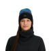 Woman wearing a black turtleneck and a striped beanie with a brand logo on a light gray background
