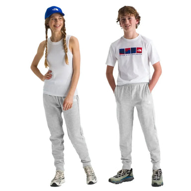 The North Face K's Camp Fleece Joggers, TNF Light Grey Heather, front view on a male and female model standing next to each other